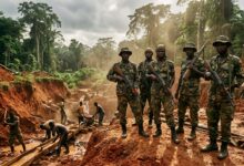 Five armed soldiers in camouflage stand guard at an open-pit mine in a tropical forest while workers dig
